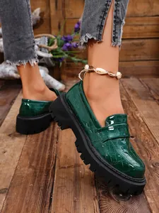 Primo piano di mocassini con plateau da donna in vernice coccodrillo verde scuro su legno