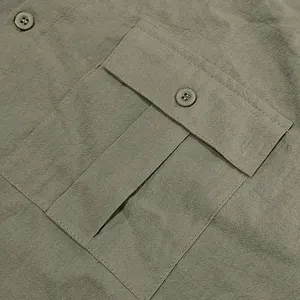 Macro view of men's olive green linen shirt pocket with button flap and texture.