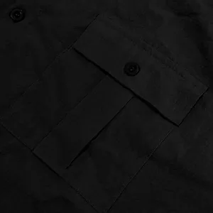 Close-up detail of a black linen shirt showing the flap pocket and fabric texture