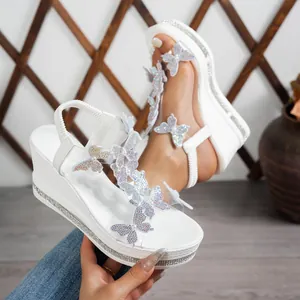 Close-up of white wedge sandals featuring sparkly butterfly and pearl embellishments.