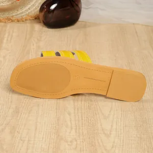 Detailansicht der rutschfesten Gummisohle der gelben flachen Damen-Strandsandalen.