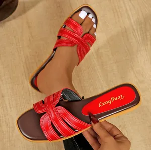 Detailaufnahme von roten flachen Sandalen mit Kreuzriemen, weißen Nähten und Karree-Zehe.