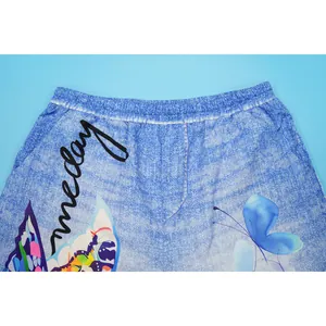 Close-up detail of blue denim-print wide-leg pants featuring butterfly and text motifs