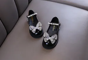 Close-up detail of girls' black patent leather shoes with shiny rhinestone butterfly decoration