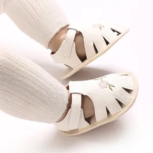 Primer plano de sandalias blancas para bebé con delicado bordado floral rosa.