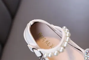 Close-up detail of girl's princess dress shoe featuring pearl strap and golden logo insole