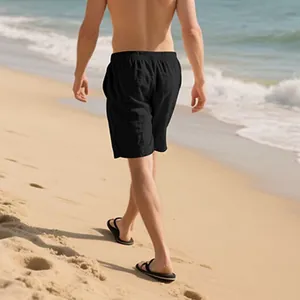 Back view of a man wearing comfortable black casual linen shorts walking on a sunny beach
