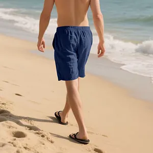 Back view of man wearing navy blue casual linen shorts walking on a sandy beach.