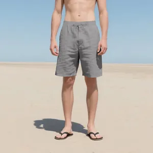 Front view of male model wearing casual grey linen shorts with drawstring on a sunny beach