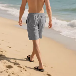 Rear view of a man walking on a beach wearing grey loose linen shorts for summer