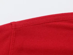 Close-up of red piqué polo shirt fabric showing breathable texture and shoulder seam