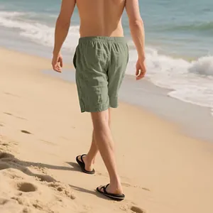 Back view of a man walking on a sandy beach wearing sage green casual linen shorts