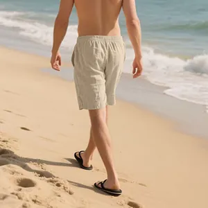 Back view of men's loose beige linen shorts worn on a sunny beach lifestyle setting.