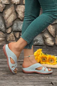 Light blue wedge sandals with floral cutout details worn in a rustic outdoor setting