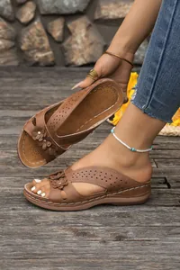 Detail view of brown wedge sandals with elegant floral cutouts and white stitching.