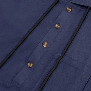 Close-up showing the textured blue linen fabric and tortoiseshell buttons of a men's shirt.