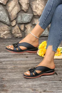 Detailed view of women's black wedge sandals with hollow floral design on feet outdoors