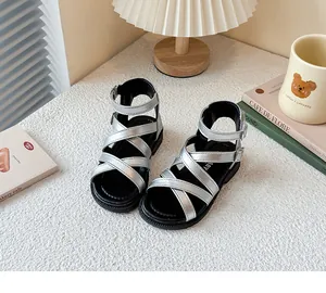 Detalle de sandalias romanas plateadas para niña con tiras cruzadas y cierre de hebilla.