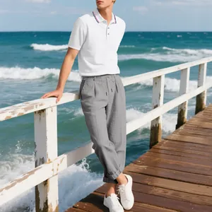 Herren-Polo-Shirt und graue Leinenhose im Set am Steg am Meer präsentiert