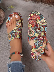 Detailed view of women's ethnic paisley print flat toe-loop sandals on foot and hand.