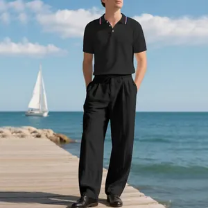 Model trägt ein schwarzes Polo-Shirt und eine Leinenhose am Meer für den Sommer.