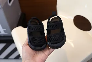 Breathable black mesh baby sandals with velcro straps held by hand for detail view.