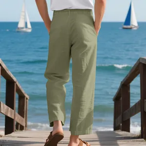 Back view of men's loose linen casual trousers in sage green at a sunny beach setting.