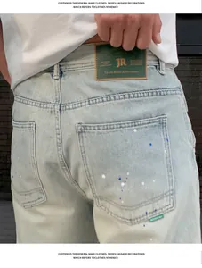 Detail of light blue men's straight jeans featuring paint splatter and brand leather patch.