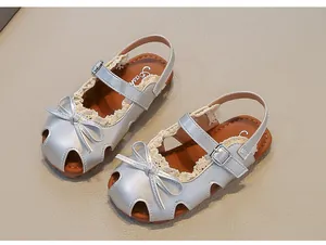 Detailaufnahme silberner Mädchensandalen mit Spitzenbesatz und feiner Schleife.