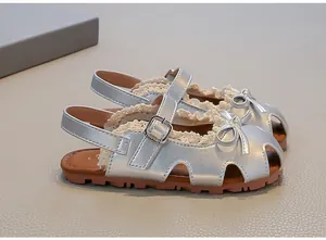 Detailansicht silberner Kindersandalen mit Schleife und zarten Spitzenbesatz-Akzenten.