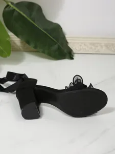 Detail view of black chunky heel sandal with anti-slip sole texture and ribbon bow