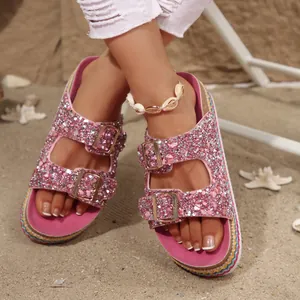 Detail view of pink glitter platform sandals with ethnic double buckle straps on beach.