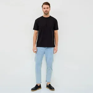Man in een minimalistisch zwart katoenen T-shirt met korte mouwen en een lichtblauwe spijkerbroek