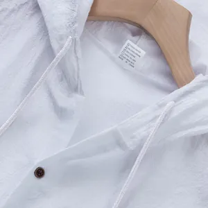 Dettaglio del gilet con cappuccio in lino bianco che mostra trama, coulisse e bottone.