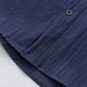 Primo piano dettagliato della trama in lino blu e del bottone in legno di una camicia da uomo.