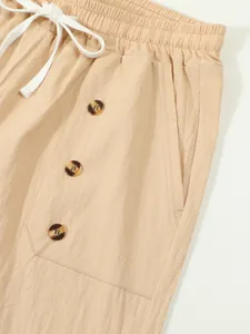 Detail of beige cotton linen shorts with tortoiseshell buttons and white drawstring.