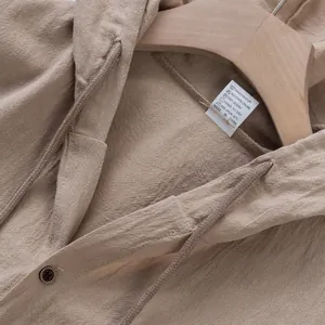 Dettaglio del gilet con cappuccio in lino kaki che mostra trama e etichetta cura