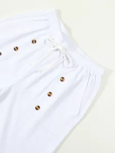 Close-up detail of white cotton linen shorts with drawstring and brown buttons
