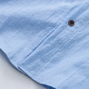 Dettaglio ravvicinato del tessuto in lino azzurro traspirante e bottone marrone su camicia estiva.
