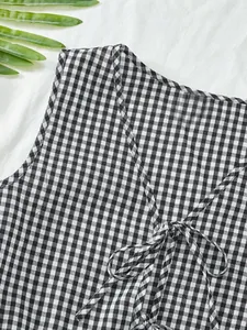 Détail d'un gilet vichy noir et blanc avec lien à nouer sur le devant et col en V.