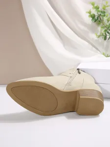 Detailed close-up of beige pointed toe ankle boot featuring chunky heel and side zipper.