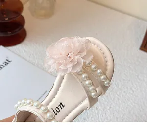 Detailopname van roze meisjessandaal met stoffen bloem en elegante parelbandjes.