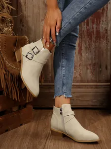 Detail of beige pointed-toe ankle boots with decorative belt buckles and block heel