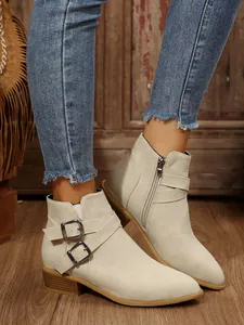 Close-up of beige pointed toe ankle boots with decorative buckle and side zipper