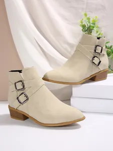 Detailed view of beige pointed-toe ankle boots with decorative double metal buckles.
