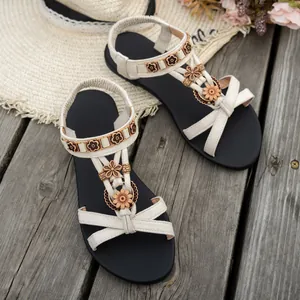Flache Bohemian-Sandalen mit Blumenverzierung und Flechtriemen auf Holzdeck