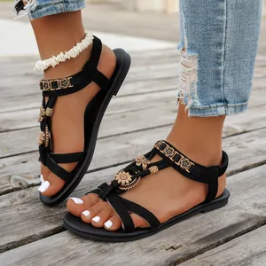 Detailansicht schwarzer flacher Sandalen im Ethno-Stil mit Blumendekor auf Holzdeck