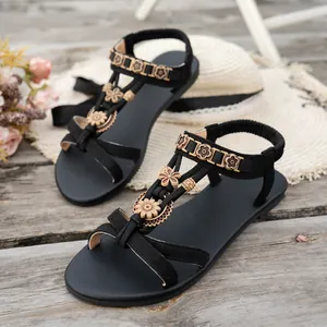Detailansicht schwarzer flacher Sandalen mit ethnischen Holzblumen-Anhängern auf Holzdeck