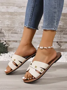 Macro-opname van crème platte sandalen met gouden studs gedragen door een model