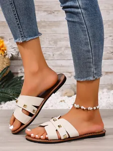 Detailopname van luxe witte slippers met gouden klinknagels en een H-riemontwerp.